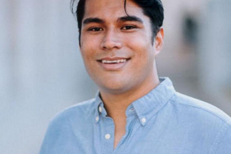Headshot of Leke Hutchins, a young Kānaka ʻŌiwi (Native Hawaiian) man. He is facing the camera and smiling. He has short black hair and an almond skin tone. He is wearing a light blue collared shirt.