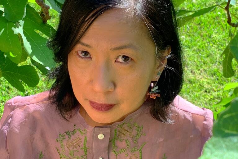 Selfie of Luisa A. Igloria, a Filipina American poet. She is outdoors and looking into the camera seriously. She has straight, shoulder-length black hair and a light almond skin tone. She is wearing colorful earrings and a mauve button-up shirt.