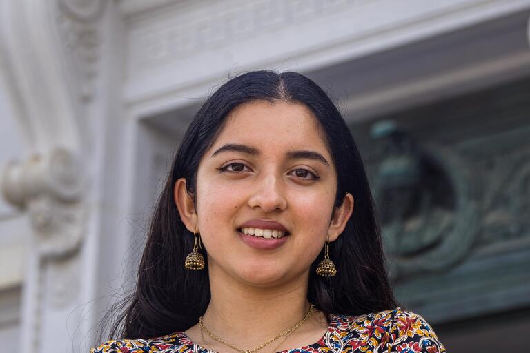 Headshot of Shreya Chaudhuri, an Indian American student at UC Berkeley. She is outside and smiling. She has long, straight black hair and a light brown skin tone. She is wearing a multi-colored collarless blouse.