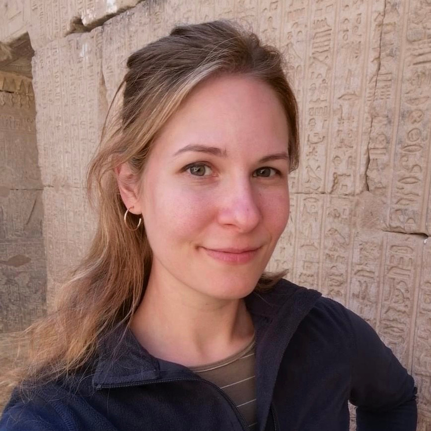 woman smiles at camera with wall engraved with hieroglyphics in the background