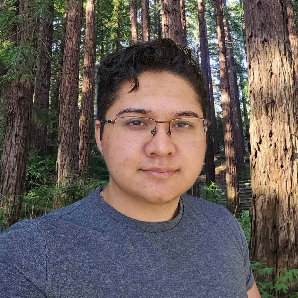 person with glasses gazes at camera with redwood trees in background