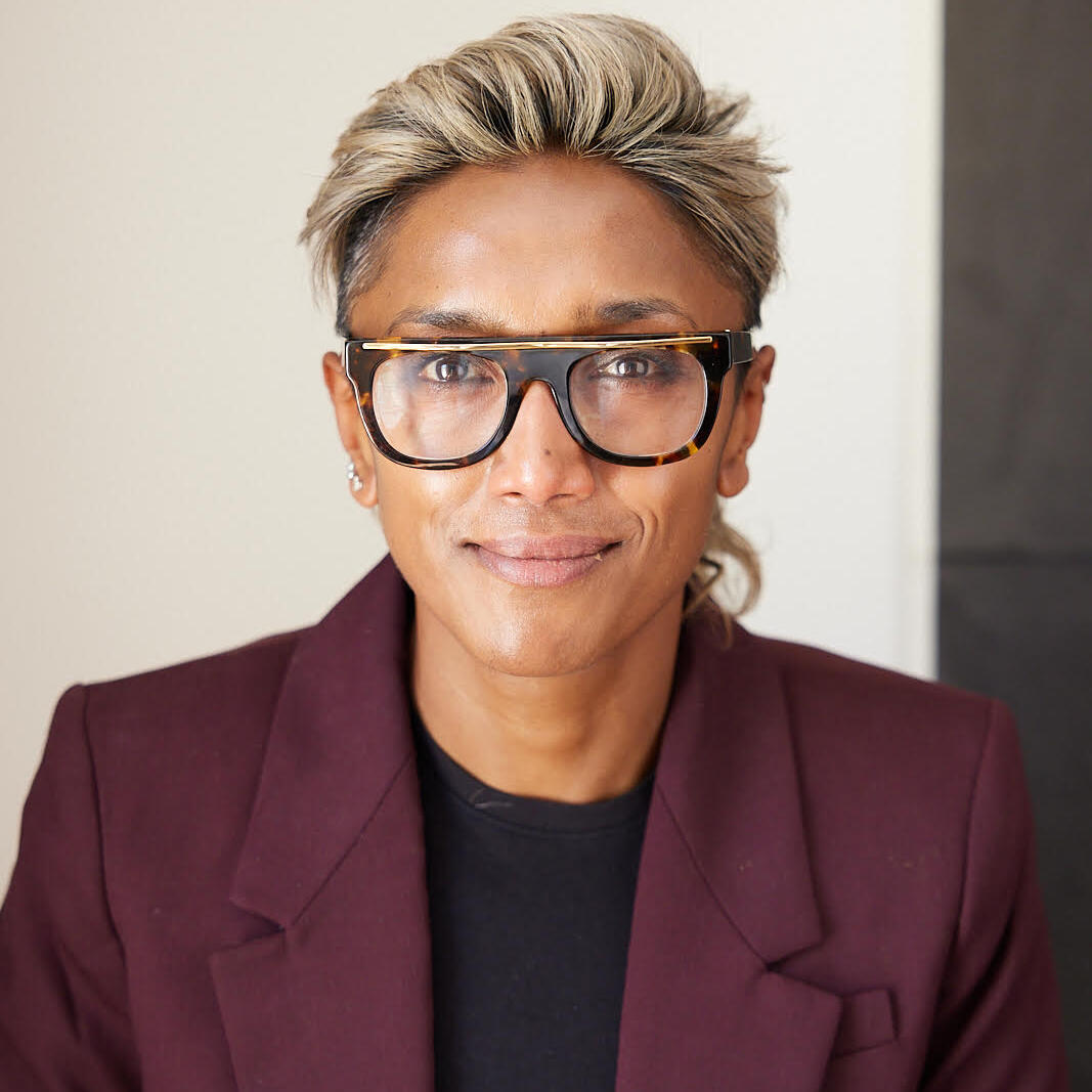 person with glasses and burgundy blazer smiles at camera