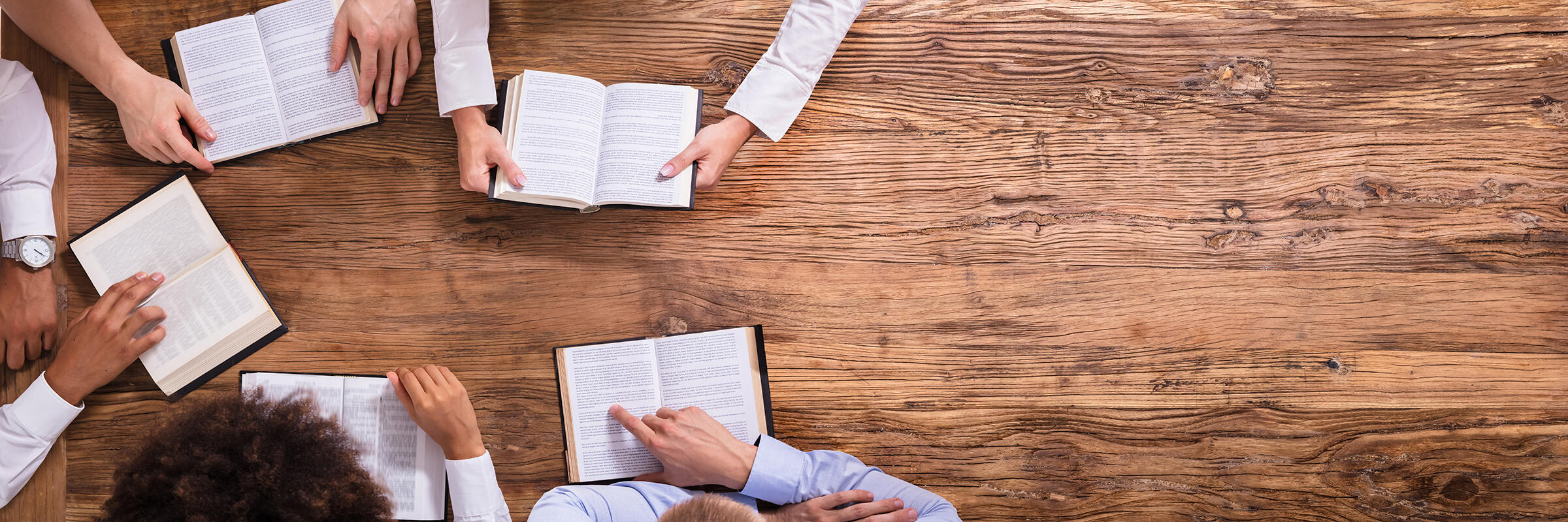 Photograph looking down at a brown wooden table with a group of people looking at books.