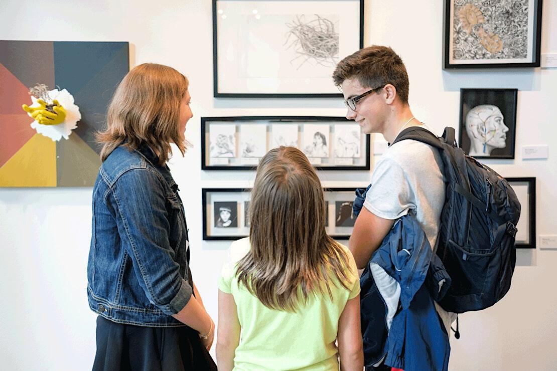Photograph of children and adults looking at arworks on a wall at a gallery.