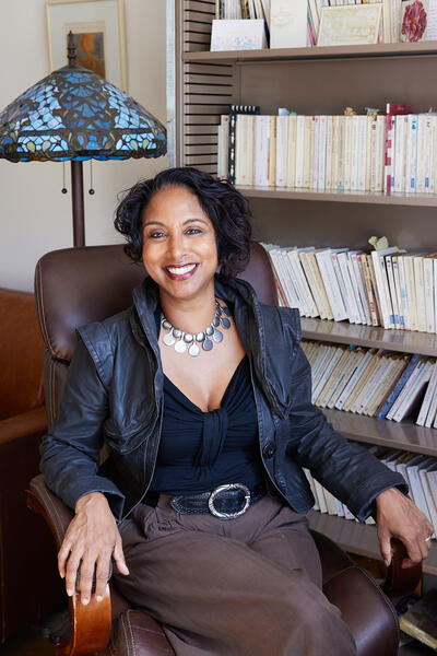 Photograph of Debarati Sanyal. She is seated in a brown leather chair. In the background is a large library shelf filled with academic books.